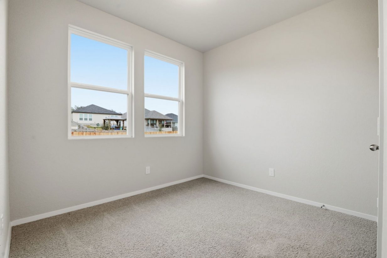 Image of a bedroom with light grey walls, tan carpeting, two windows and white trim