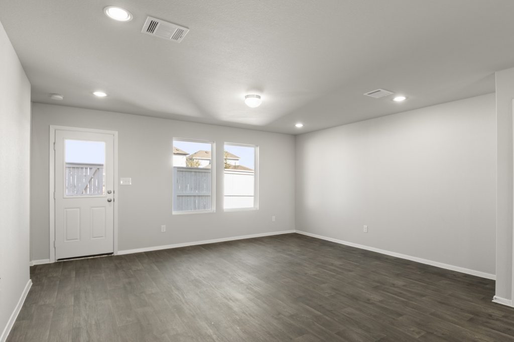 Image of a living room with dark vinyl flooring, light grey walls, two windows and a white back door