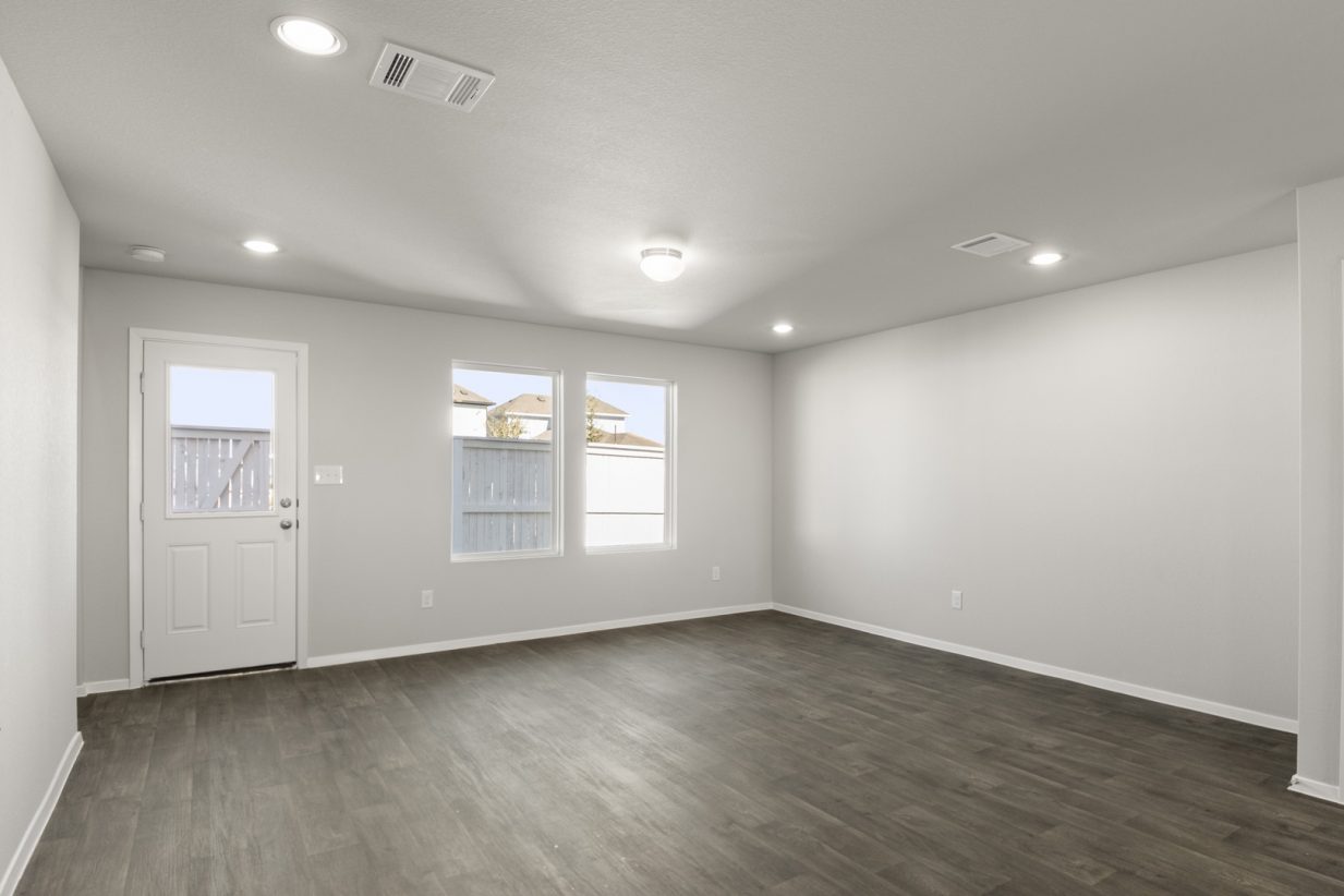 Image of a living room with dark vinyl flooring, light grey walls, two windows and a white back door