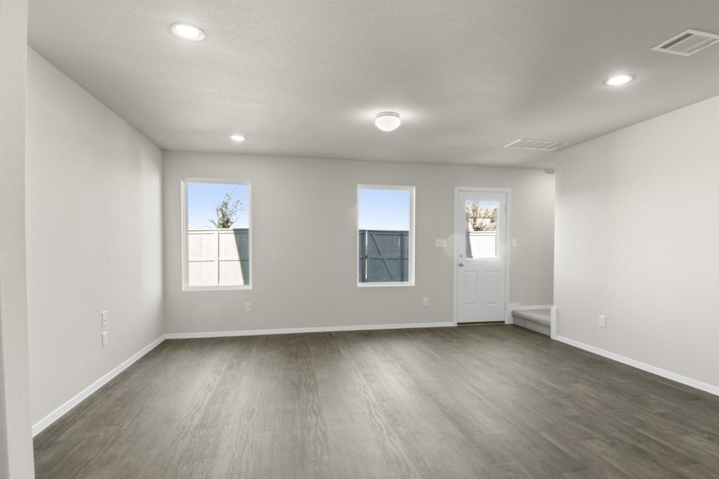 Image of a living room with dark brown vinyl flooring, light grey walls, two windows and a white backdoor