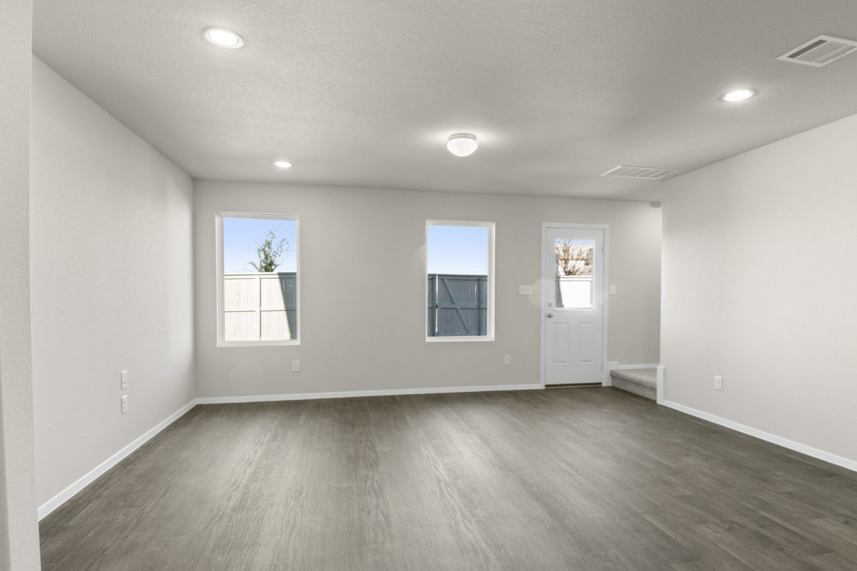 Image of a living room with dark brown vinyl flooring, light grey walls, two windows and a white backdoor