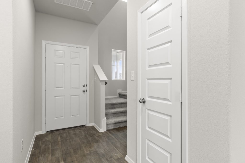 Image of two story home foyer with brown flooring and light grey walls and carpeted stairs