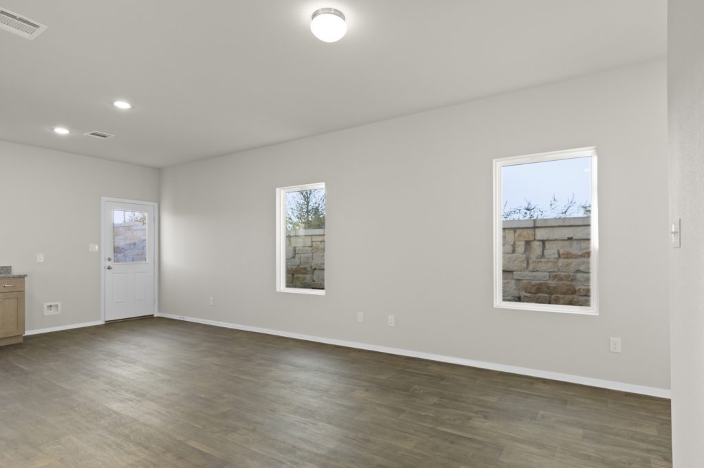 Image of a one story home living room with dark wood-like flooring and light grey walls with windows