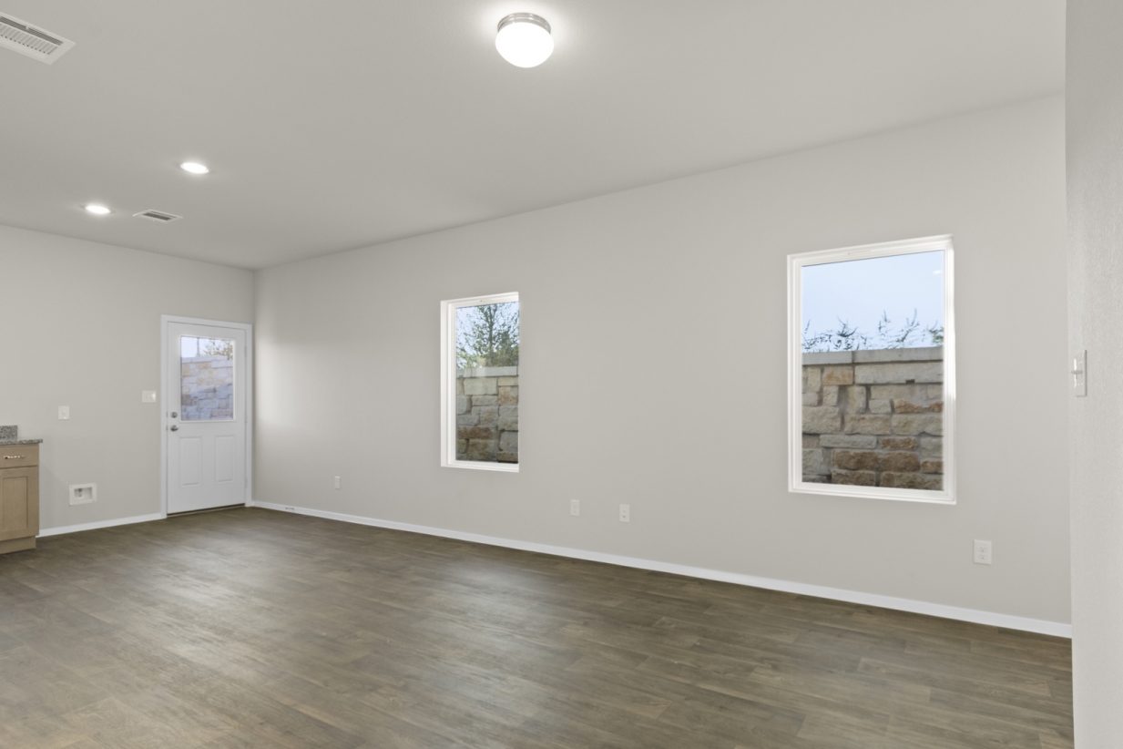 Image of a one story home living room with dark wood-like flooring and light grey walls with windows