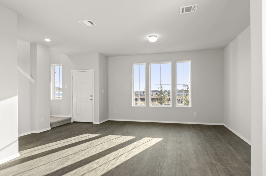 Image of a living room with brown wood-like flooring with light grey painted walls with three windows