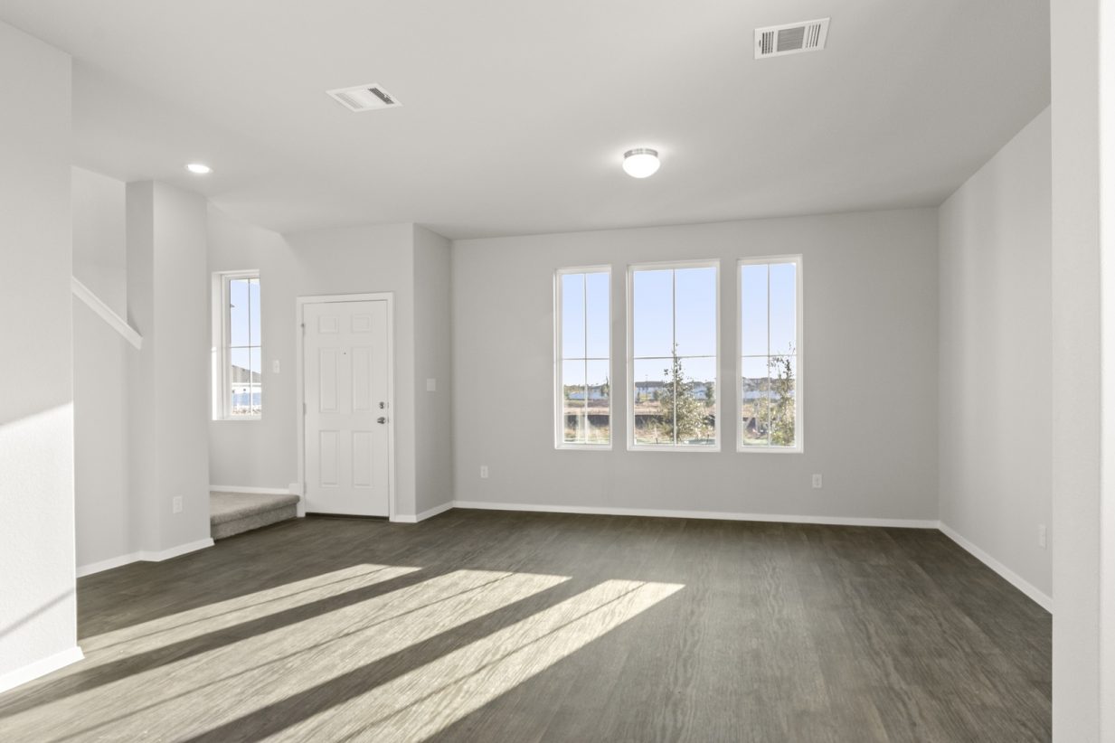 Image of a living room with brown wood-like flooring with light grey painted walls with three windows