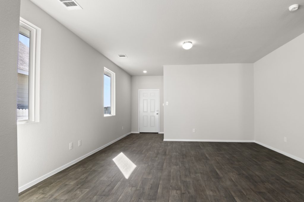 Image of a living room with light grey walls, dark brown flooring, white trim and a white front door