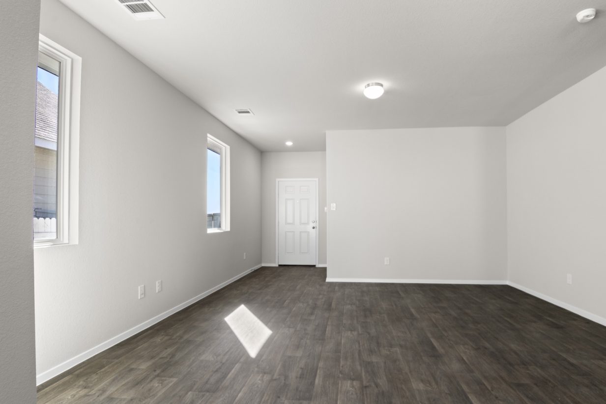 Image of a living room with light grey walls, dark brown flooring, white trim and a white front door