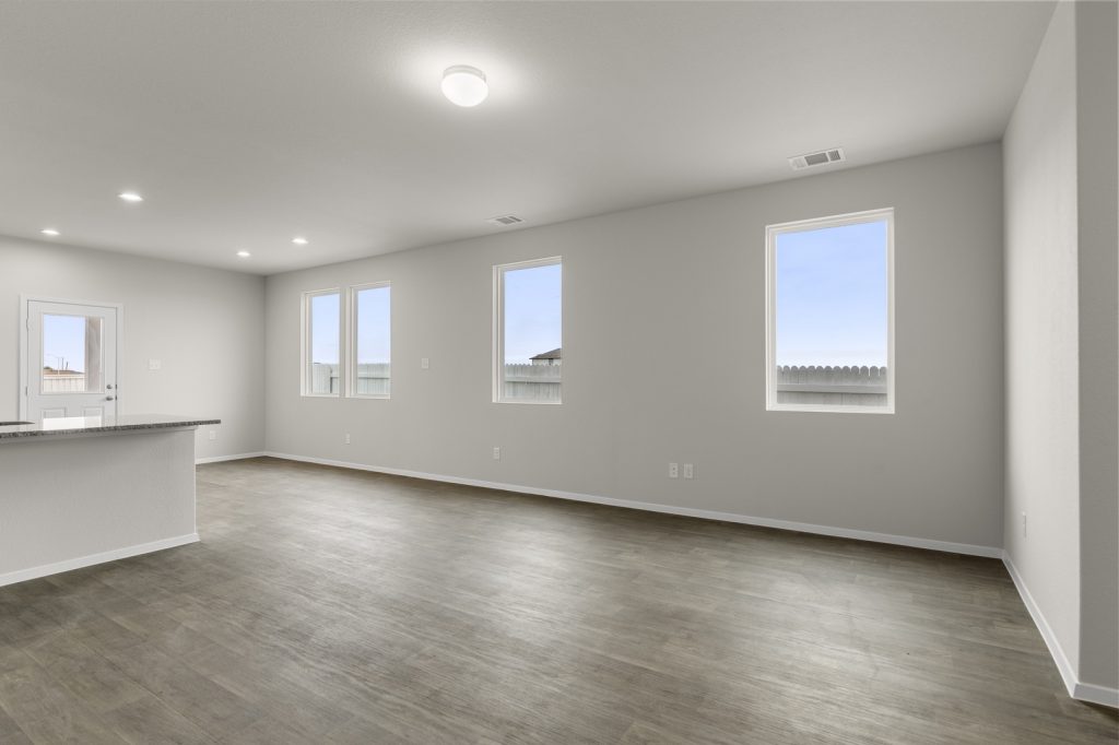 Image of a living room with cream walls, dark brown vinyl flooring, windows and white trim