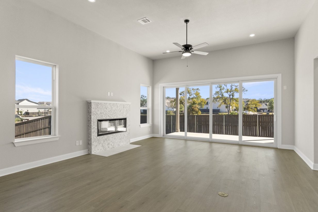 Image of two story home living room with wooden flooring and light grey painted walls with windows and a sliding glass door that leads to the backyard