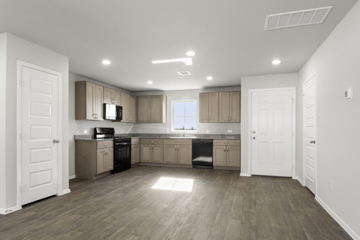 Image of a L-shaped kitchen with brown cabinets, granite countertops, black appliances and a sink above the winodw