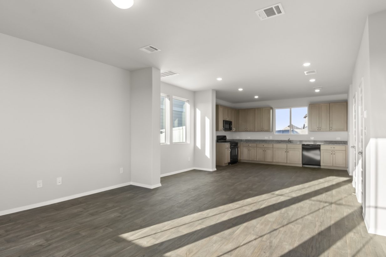 Image of living and dining room area with dark brown wood-like flooring and light grey painted walls with a kitchen in the distance