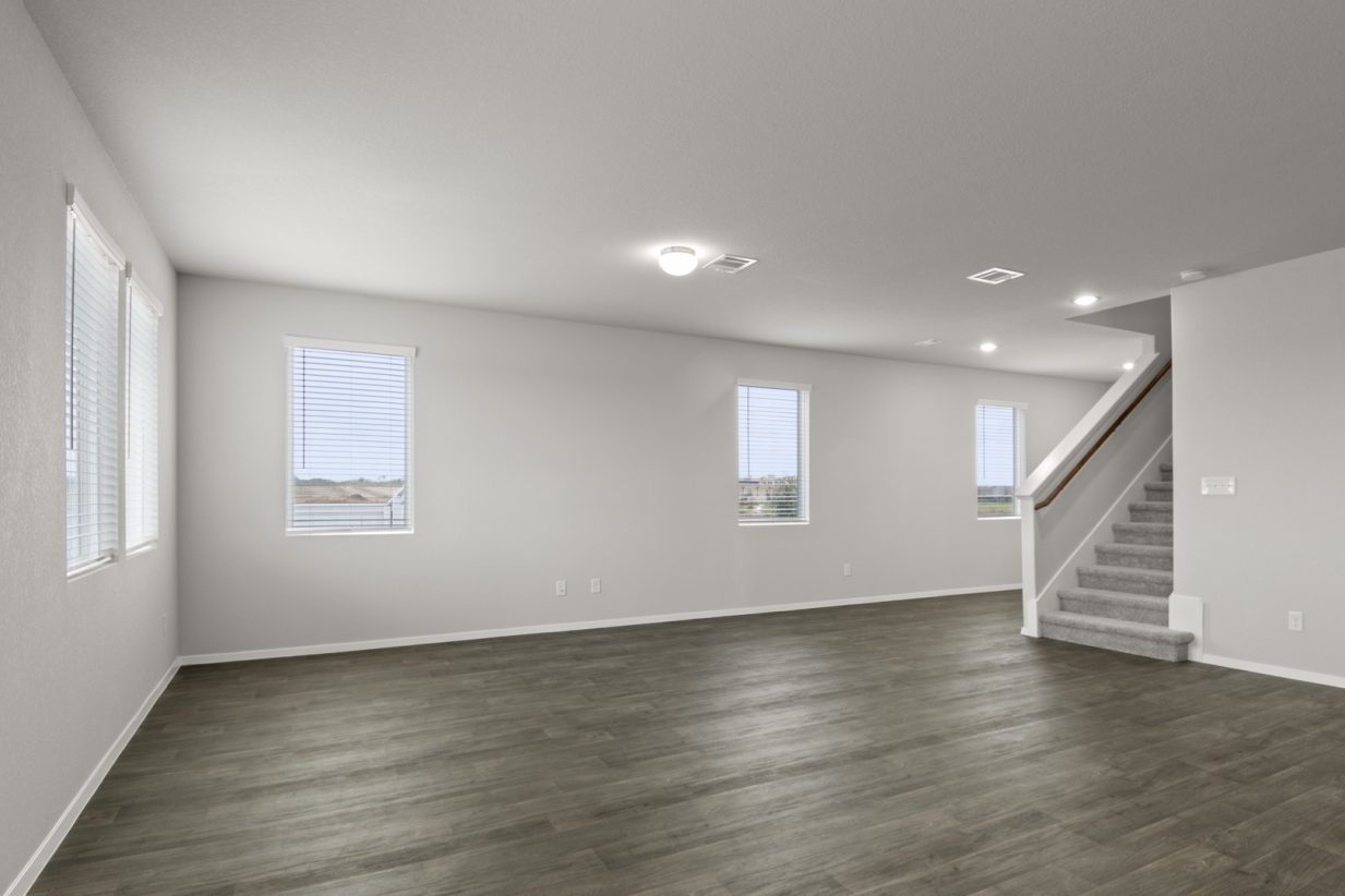 Image of a living room with dark vinyl flooring, grey walls, and a carpeted staircase that leads upstairs