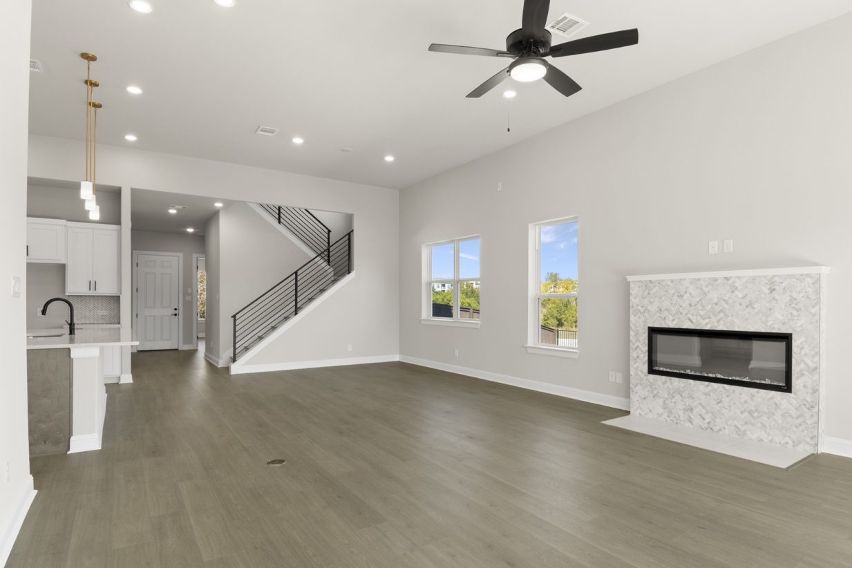 Image of a two story home living room with light wood flooring and light grey painted walls with a brick electric fireplace and ceiling fan