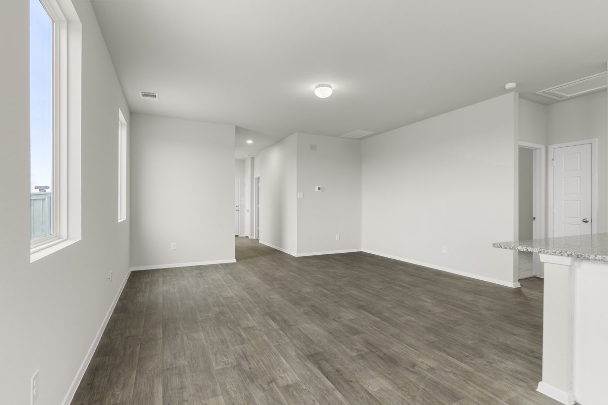 Image of a living room with cream walls, dark brown vinyl flooring, windows and white trim