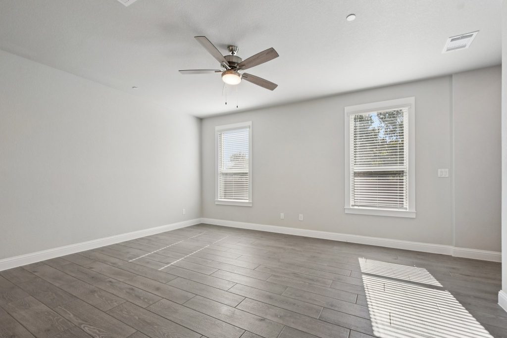 Image of a living room with light grey walls, windows, white trim and a ceiling fan