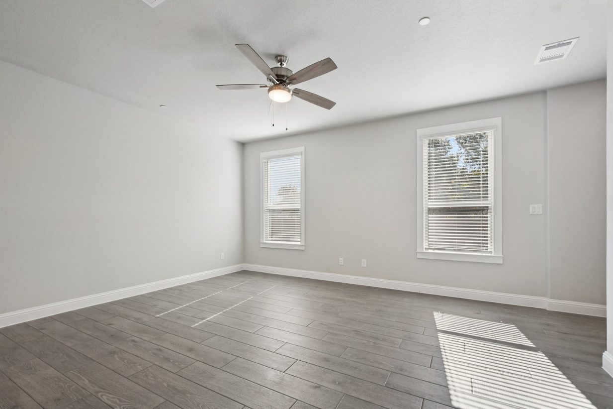 Image of a living room with light grey walls, windows, white trim and a ceiling fan