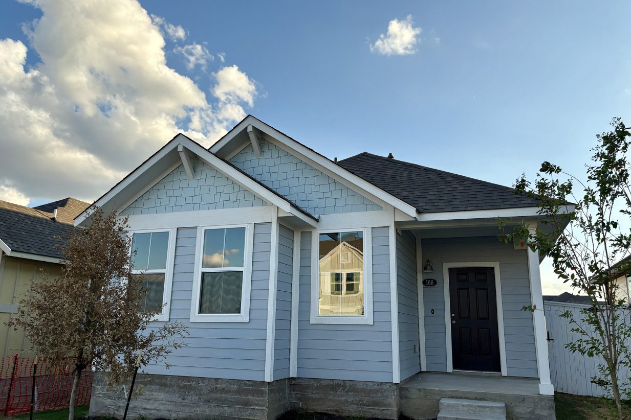 Image of one-story two-tone blue home with white trim and black front door with green grass and sky
