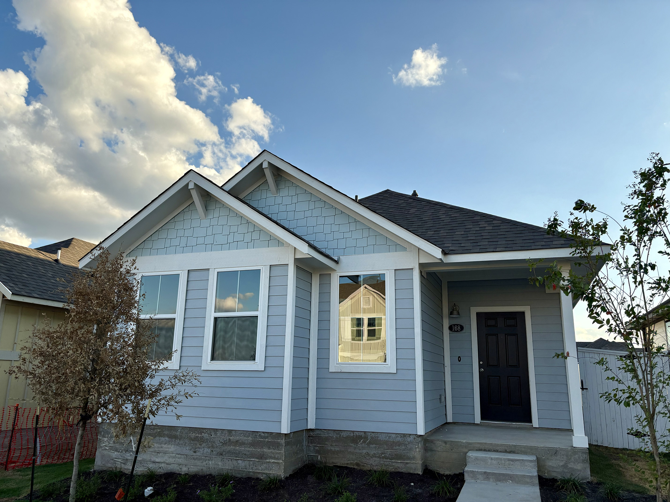 Image of one-story two-tone blue home with white trim and black front door with green grass and sky