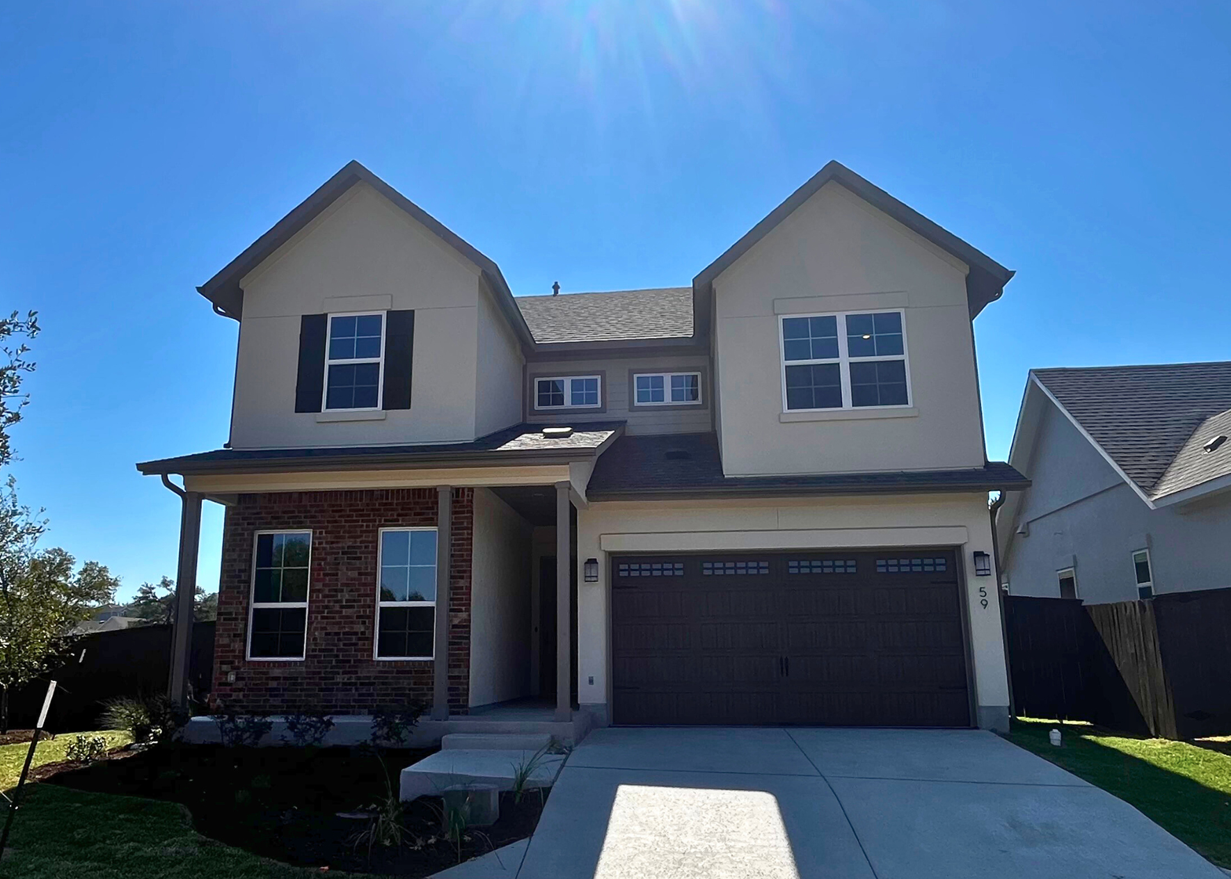 Image of the front exterior of two-story house with brick accents, concrete drive, a grass landscape, and blue sky.