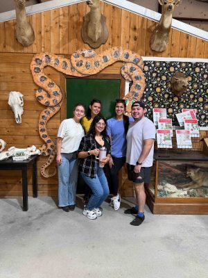 Image of a group of people inside with a snake decoration and wood paneling wall and concrete floor.