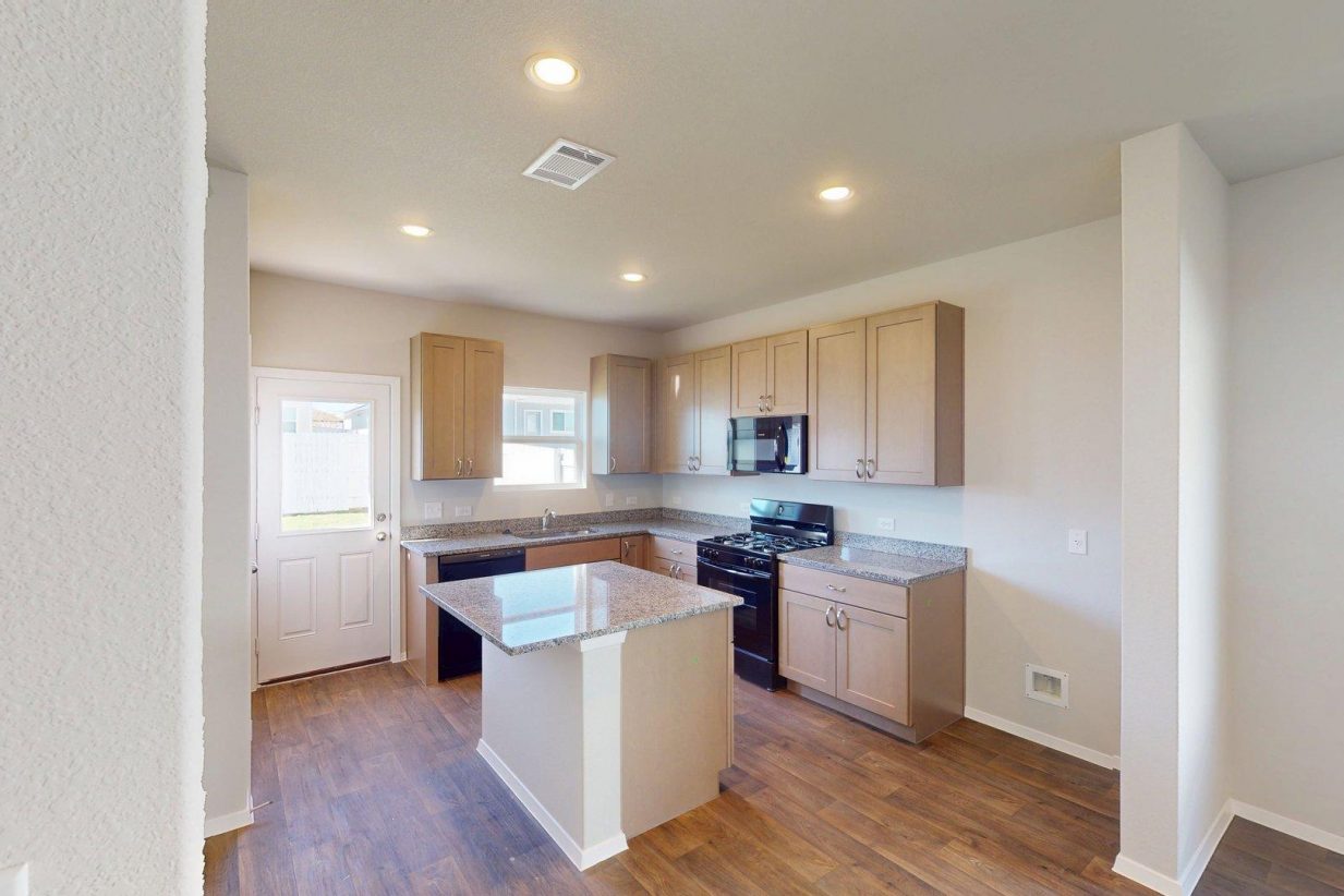 Image of a kitchen with a center island with granite counter tops, brown cabinets and black appliances