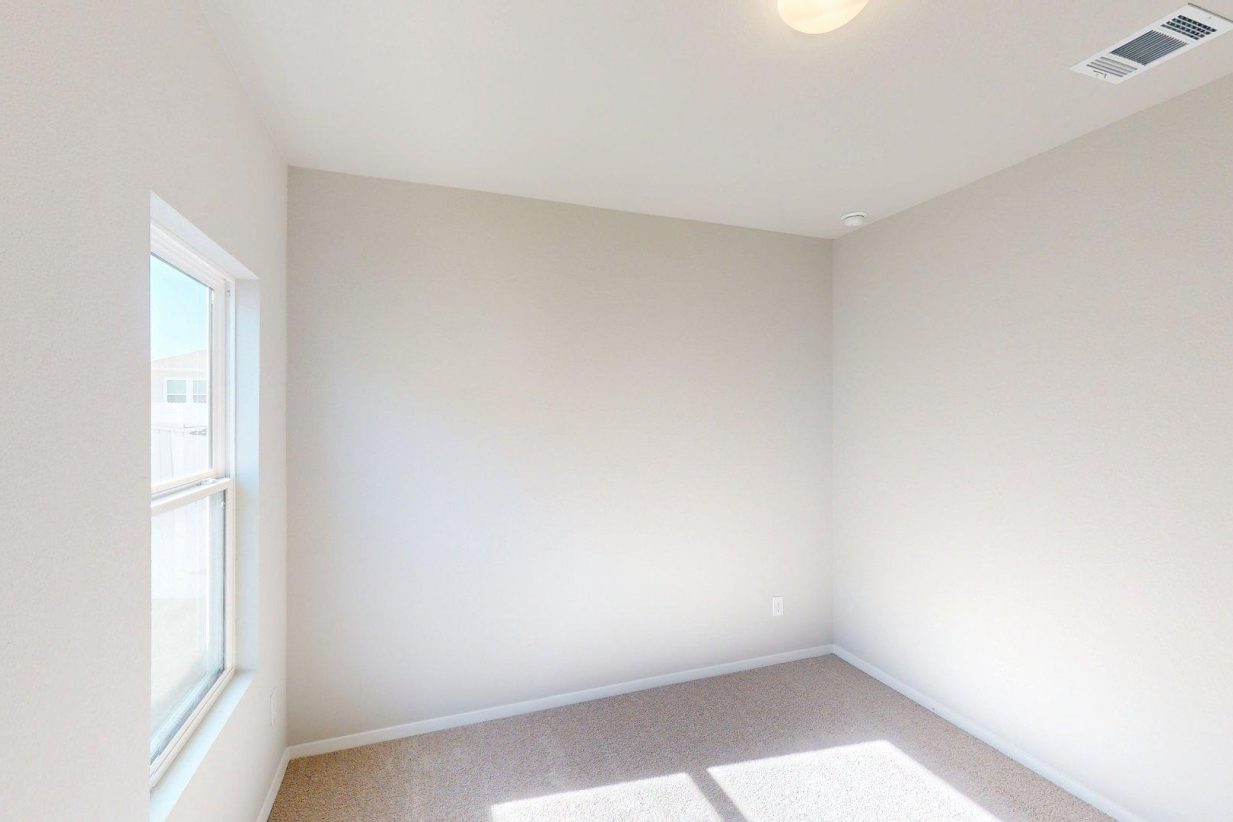 Image of a bedroom with tan carpeting and light grey painted walls and a window