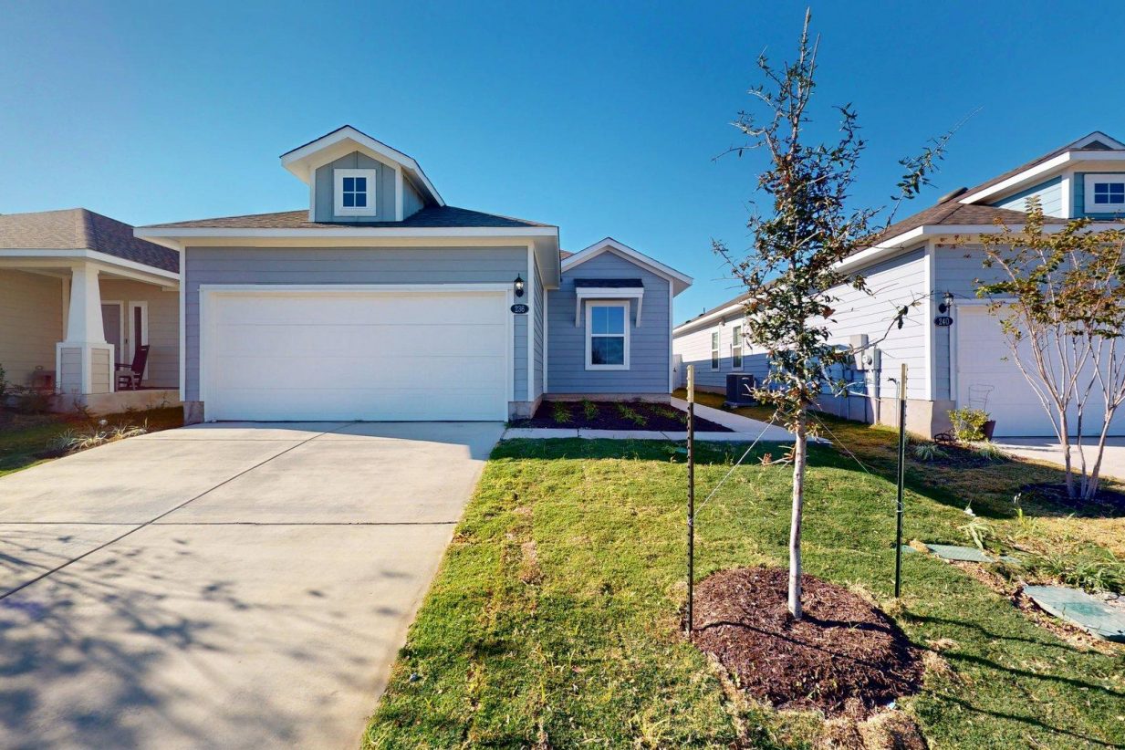 Image of a one story home with a two car garage and a cement driveway with green grass and a blue sky