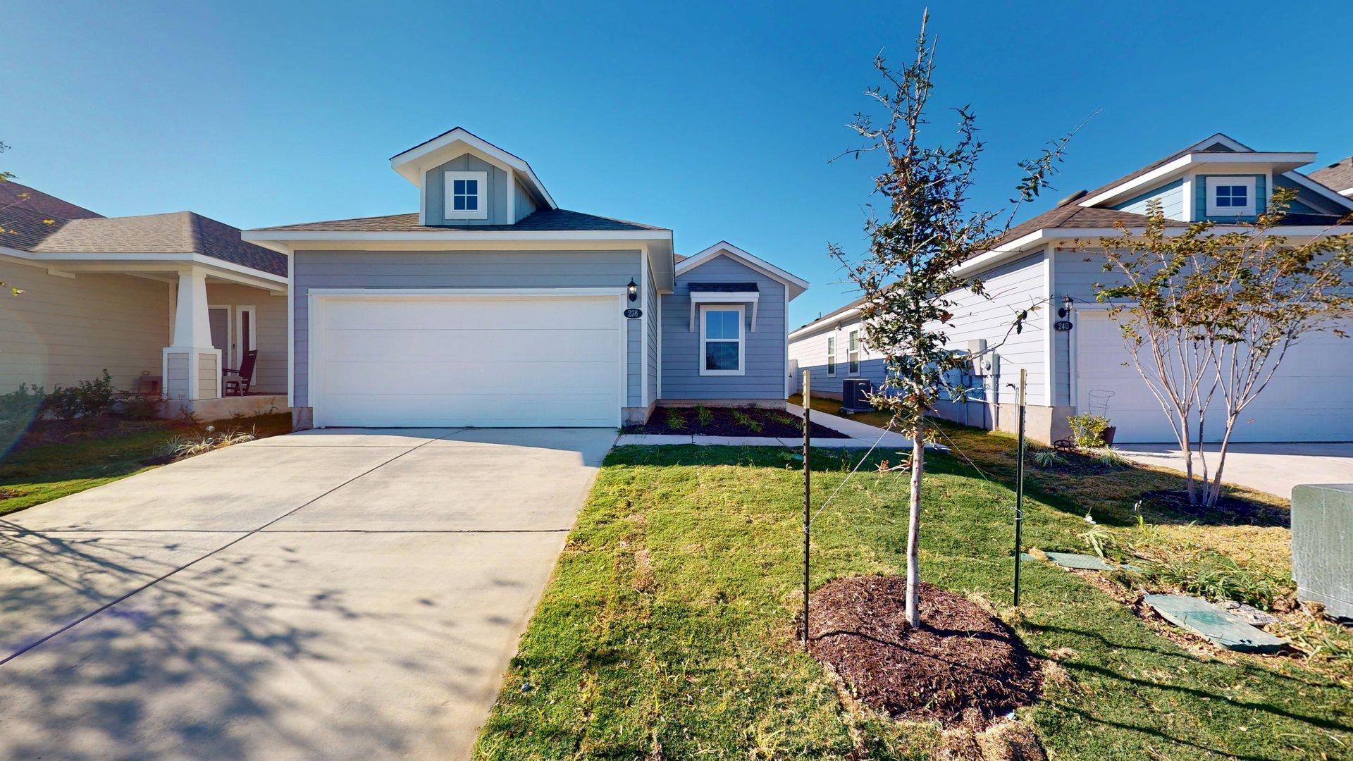 Image of a one story home with a two car garage and a cement driveway with green grass and a blue sky