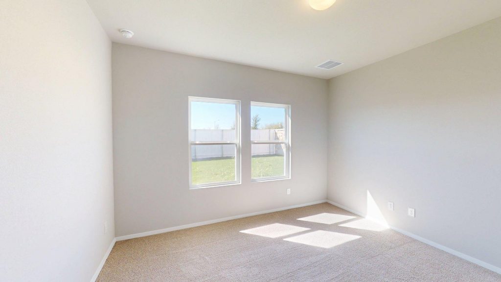Image of a one story home bedroom with tan carpeting and light grey walls with two windows