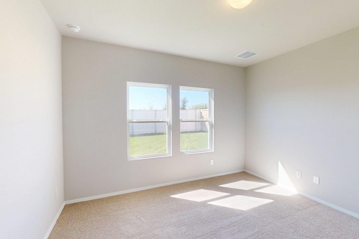 Image of a one story home bedroom with tan carpeting and light grey walls with two windows