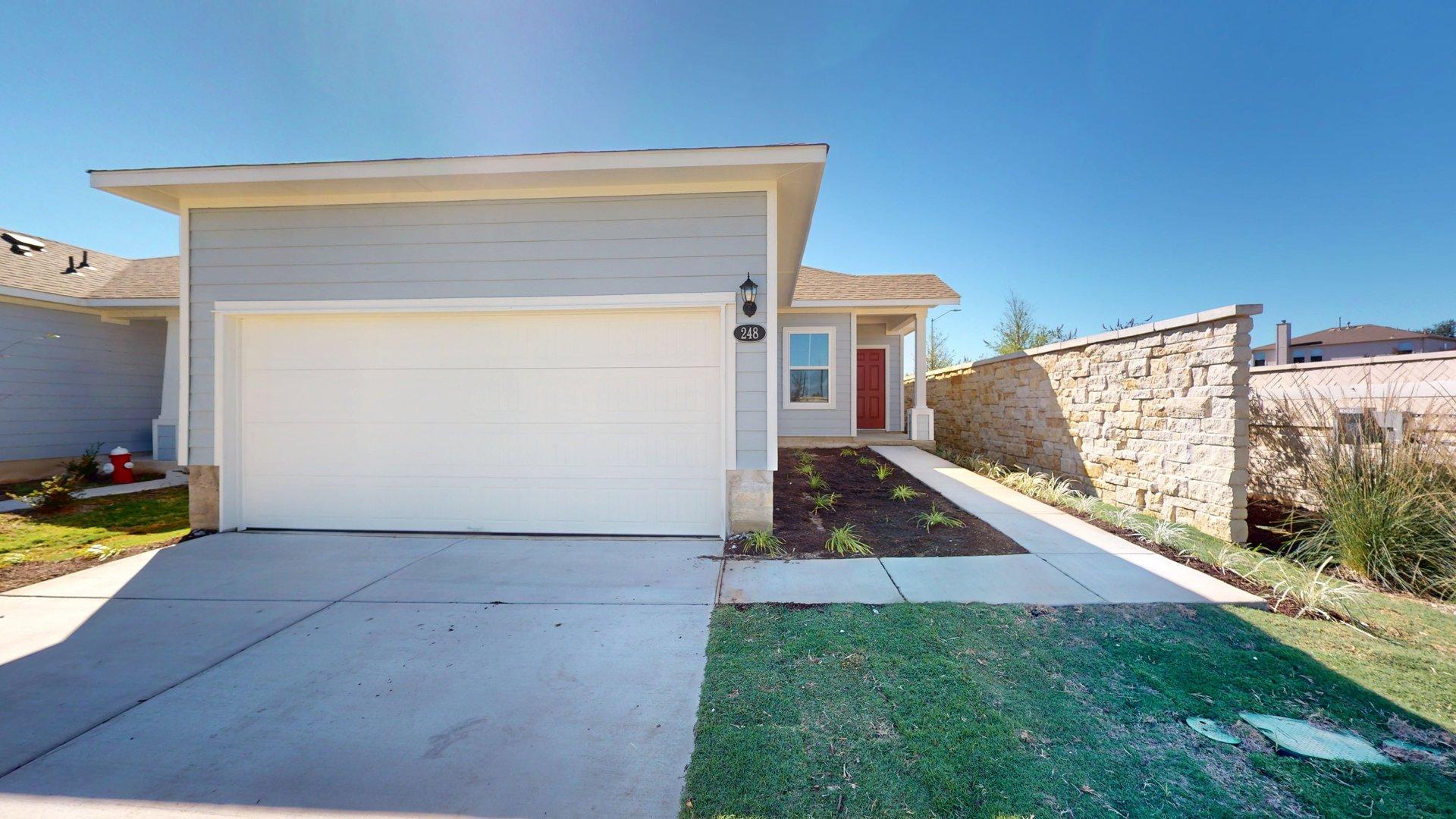 Image of exterior grey one story home with a red door and white two car garage with a cement driveway and a blue sky
