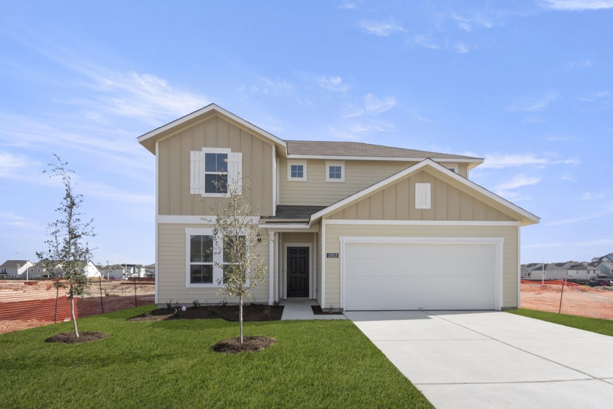 Image of a front exterior of a tan two story house with a black front door, white trim and garage door, green grass front yard, a cement driveway and a blue sky in the background