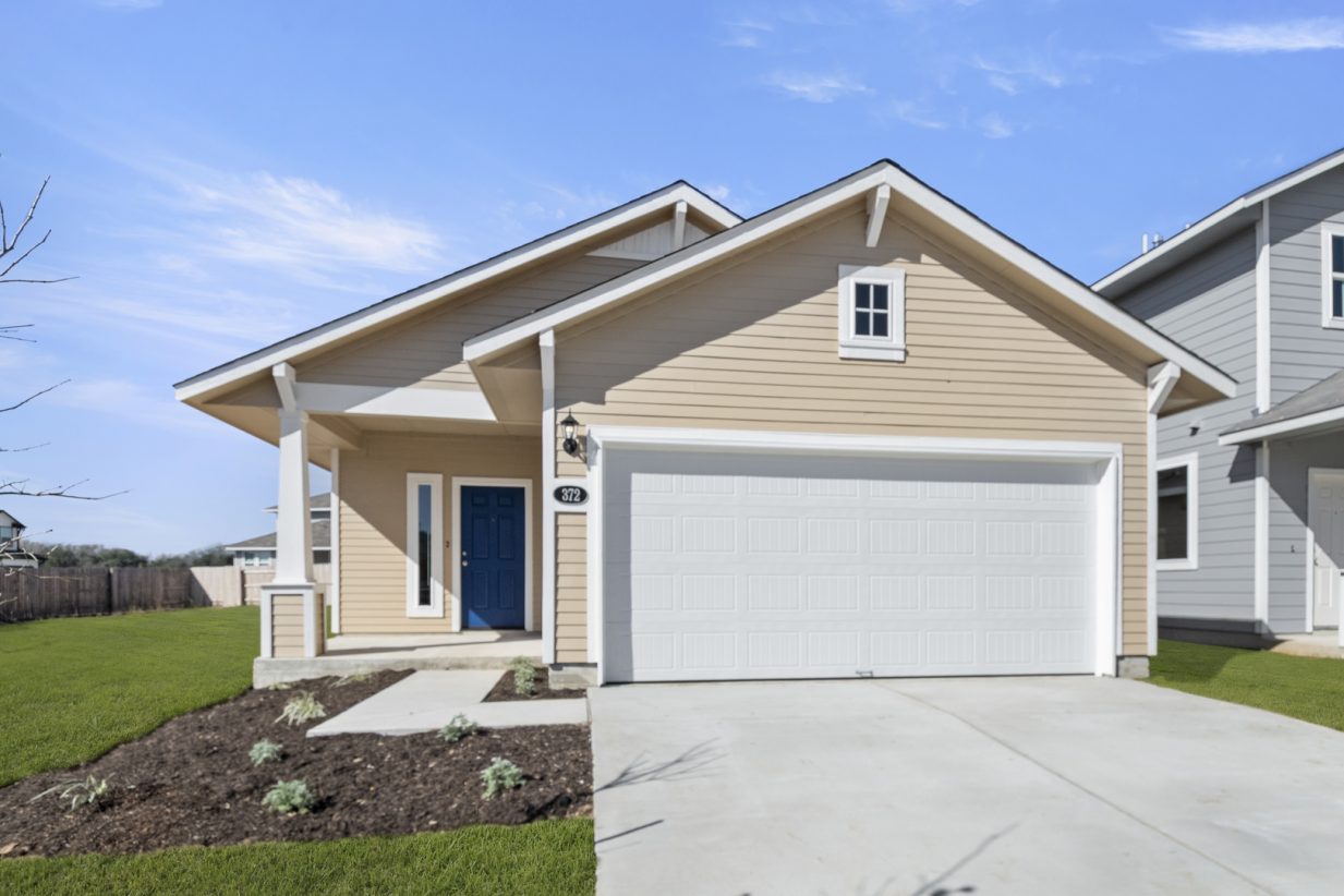 Image of a beige one story house with a white garage, white trim, a royal blue front door, cement driveway, a green grass backyard and a blue sky in the background