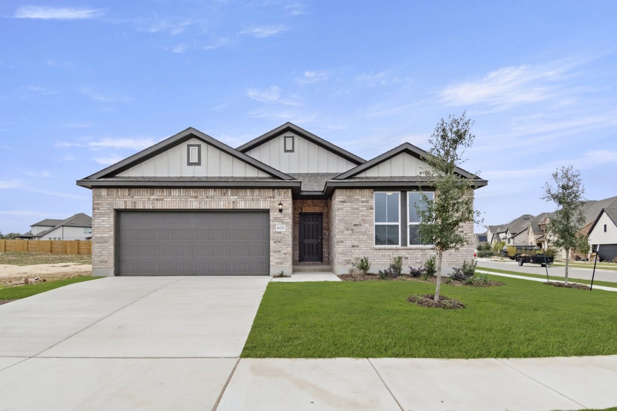 Image of a one story brick home exterior with a blue door, brown garage and a cement driveway