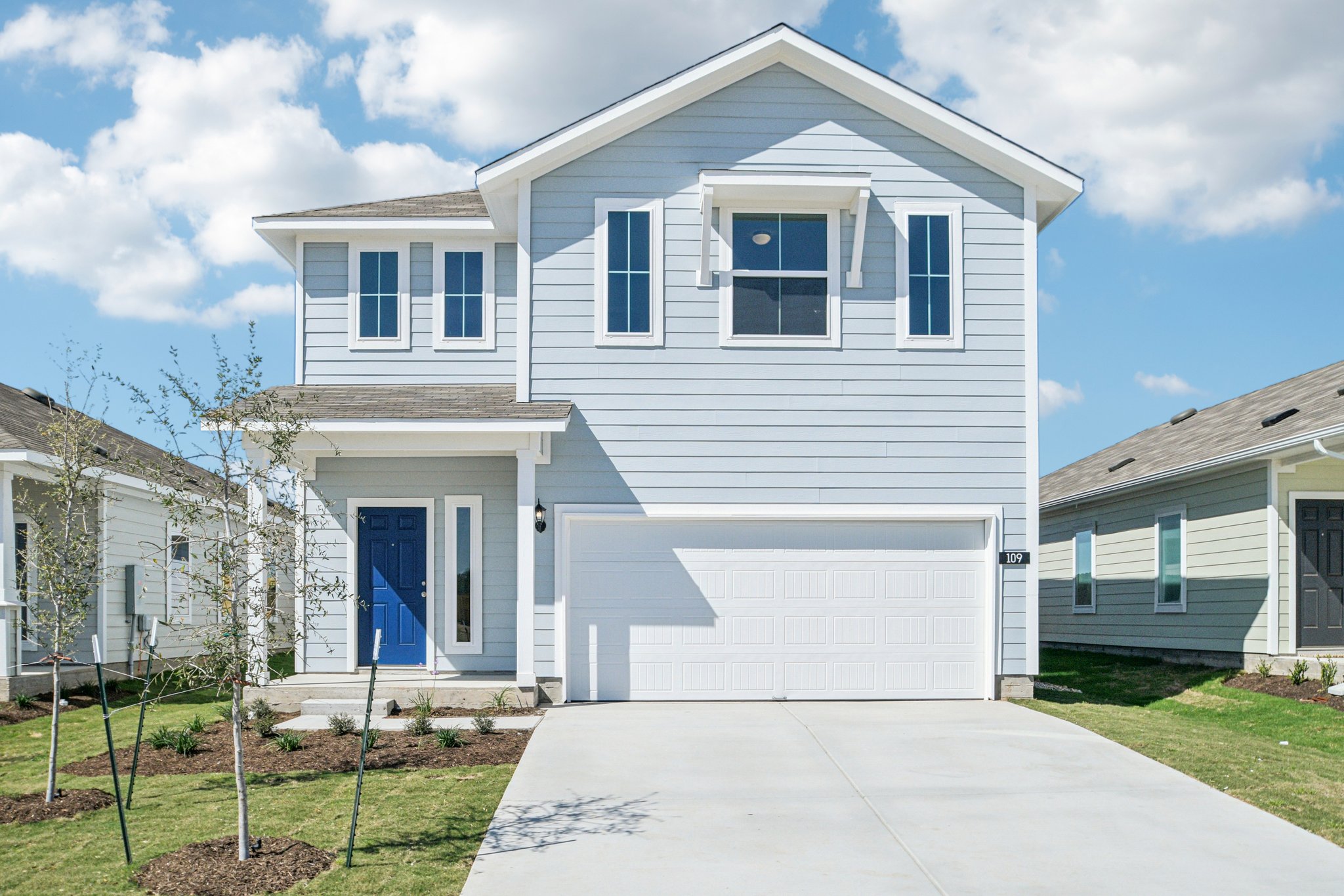 Image of a blue two story house with a white garage, blue front door, cement driveway and a blue sky in the background