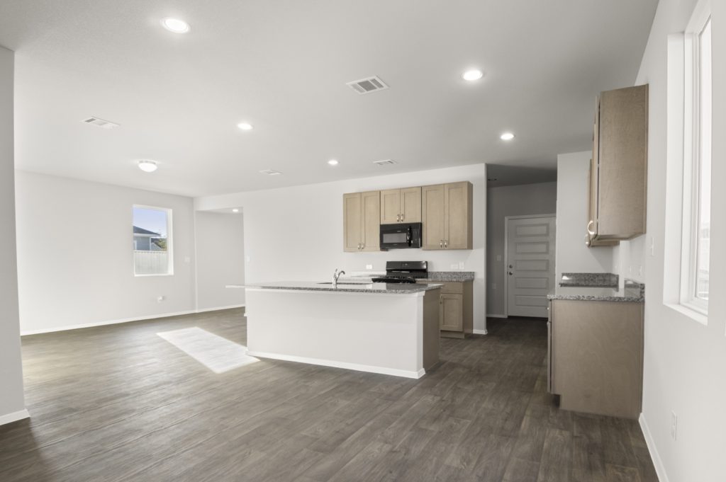 Image of a dining room with brown wood-like flooring with a open kitchen