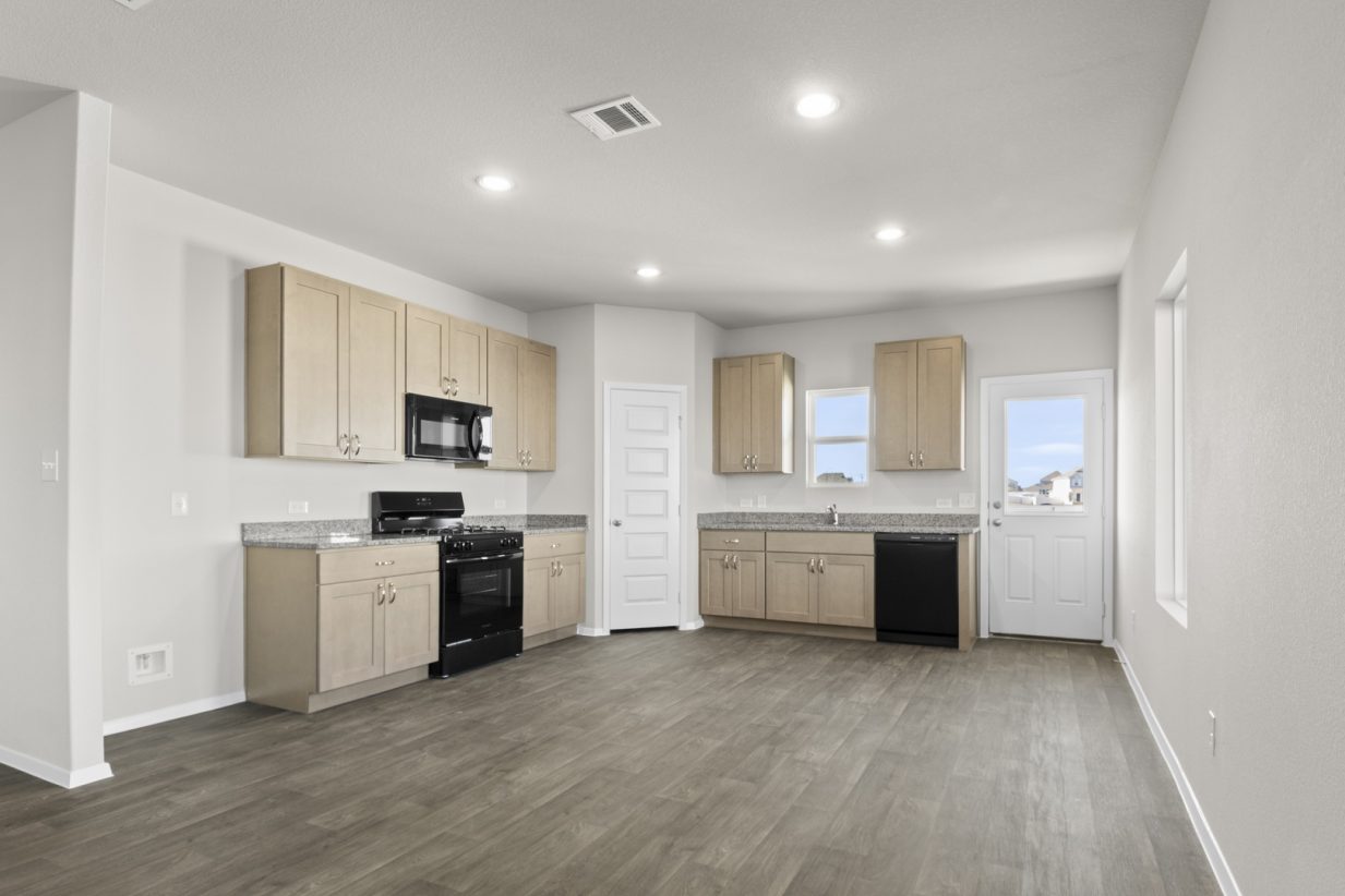 Image of a kitchen and dining room with light brown cabinets, granite countertops, and black kitchen appliances