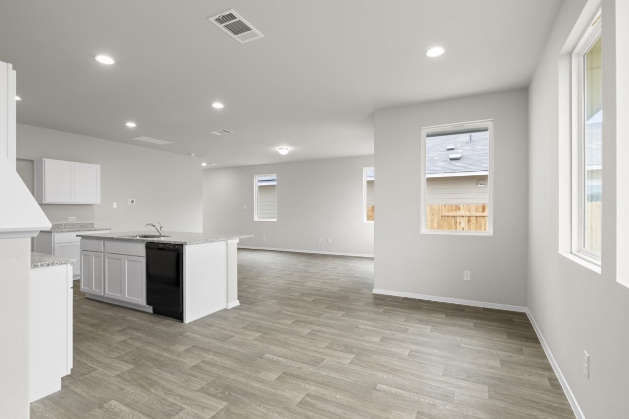 Image of a dining room area with a kitchen to the lest, cream walls, light brown flooring and windows