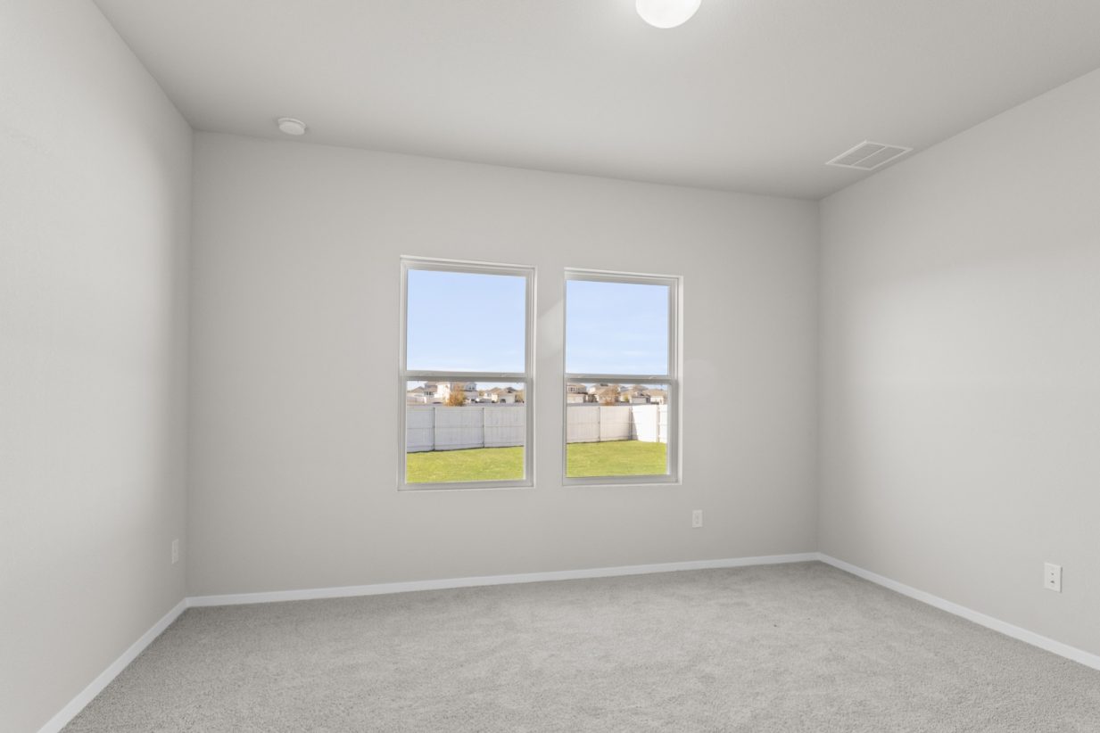 Image of a primary bedroom with tan carpeting and light grey walls with two windows