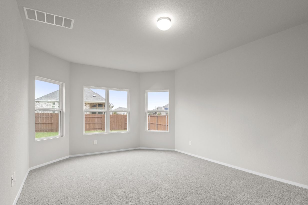 Image of a primary bedroom with tan carpeting, light grey walls and three windows
