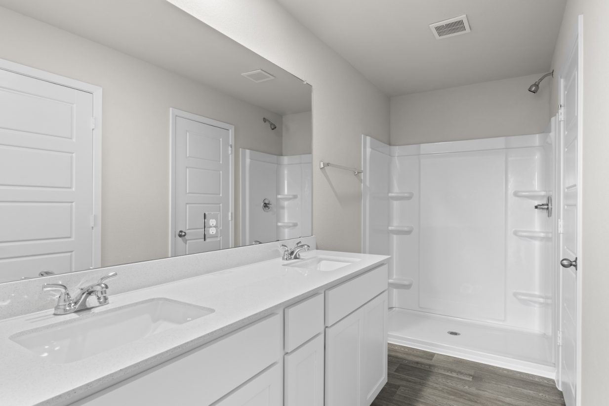 Image of a bathroom with a white jack and jill vanity, white cabinets, a large mirror, and a walk-in shower