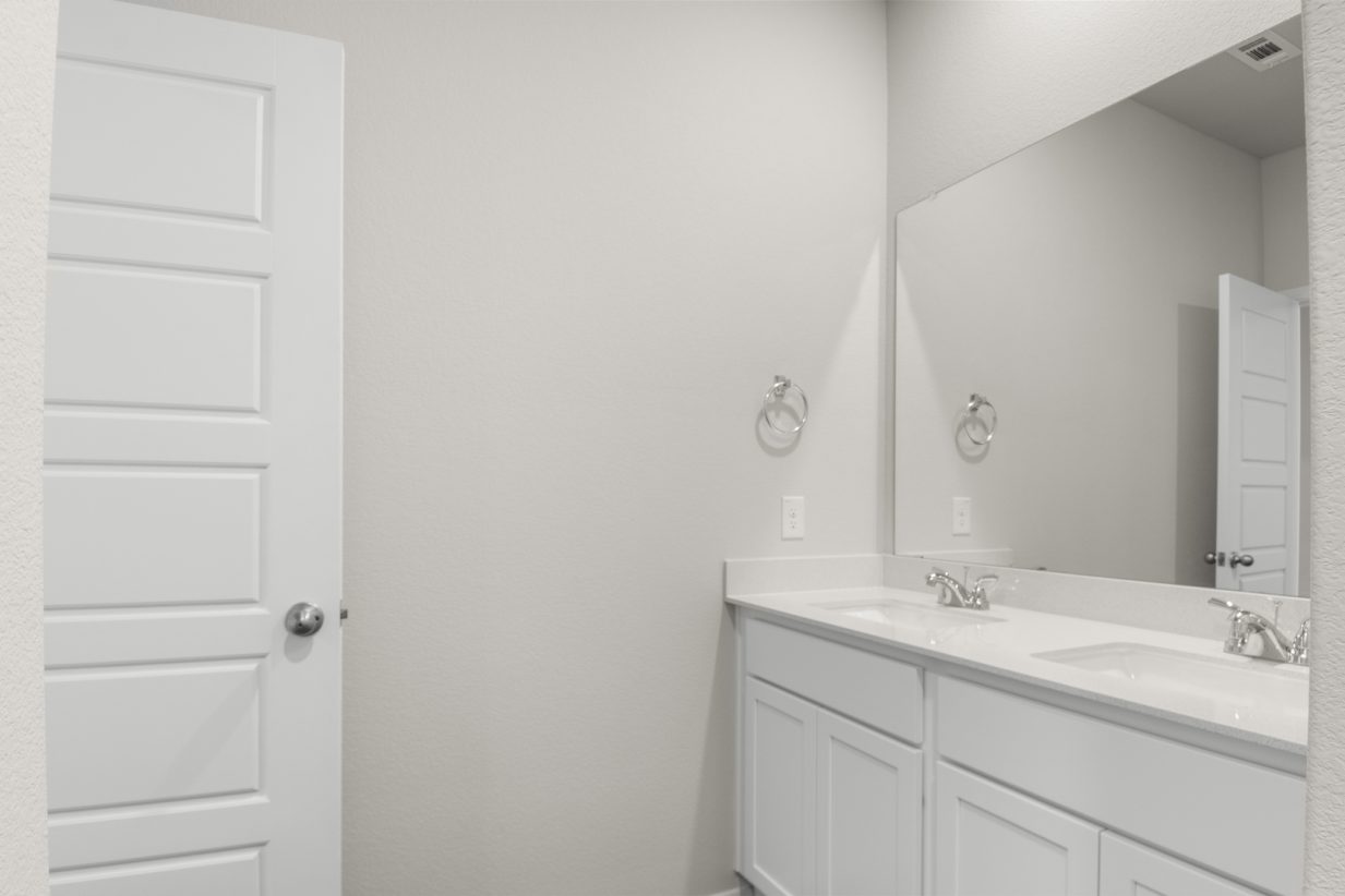 Image of a primary bathroom with cream walls, white cabinets and jack and jill vanity, and a large mirror