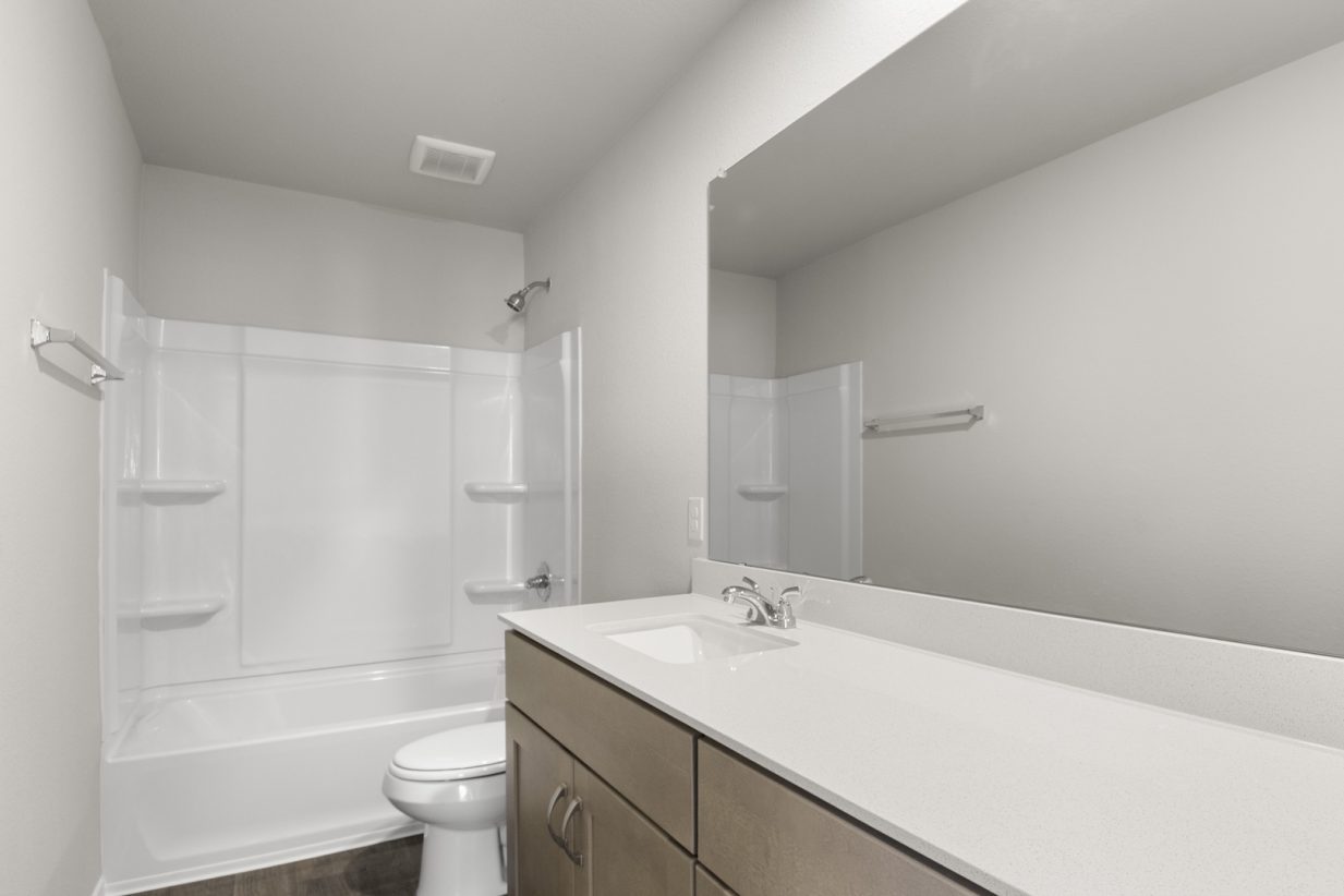 Image of a bathroom with a large mirror, a dual white vanity, white shower and tub, and light brown cabinets