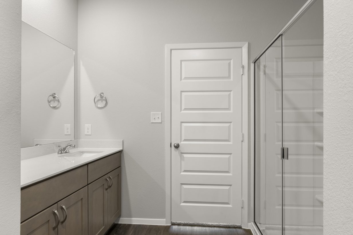 Image of a primary bathroom with brown cabinets, a white vanity and a white vinyl walk-in shower