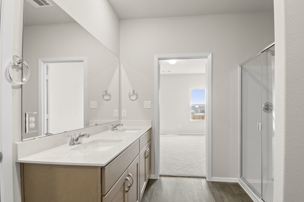 Image of a primary bedroom with light brown cabinets, a white double vanity, a large mirror, and a standing shower