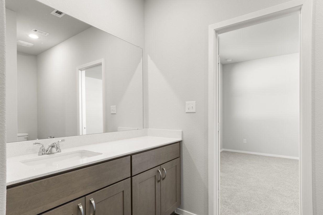 Image of a primary bathroom with brown cabinets and white vanity with a large mirror
