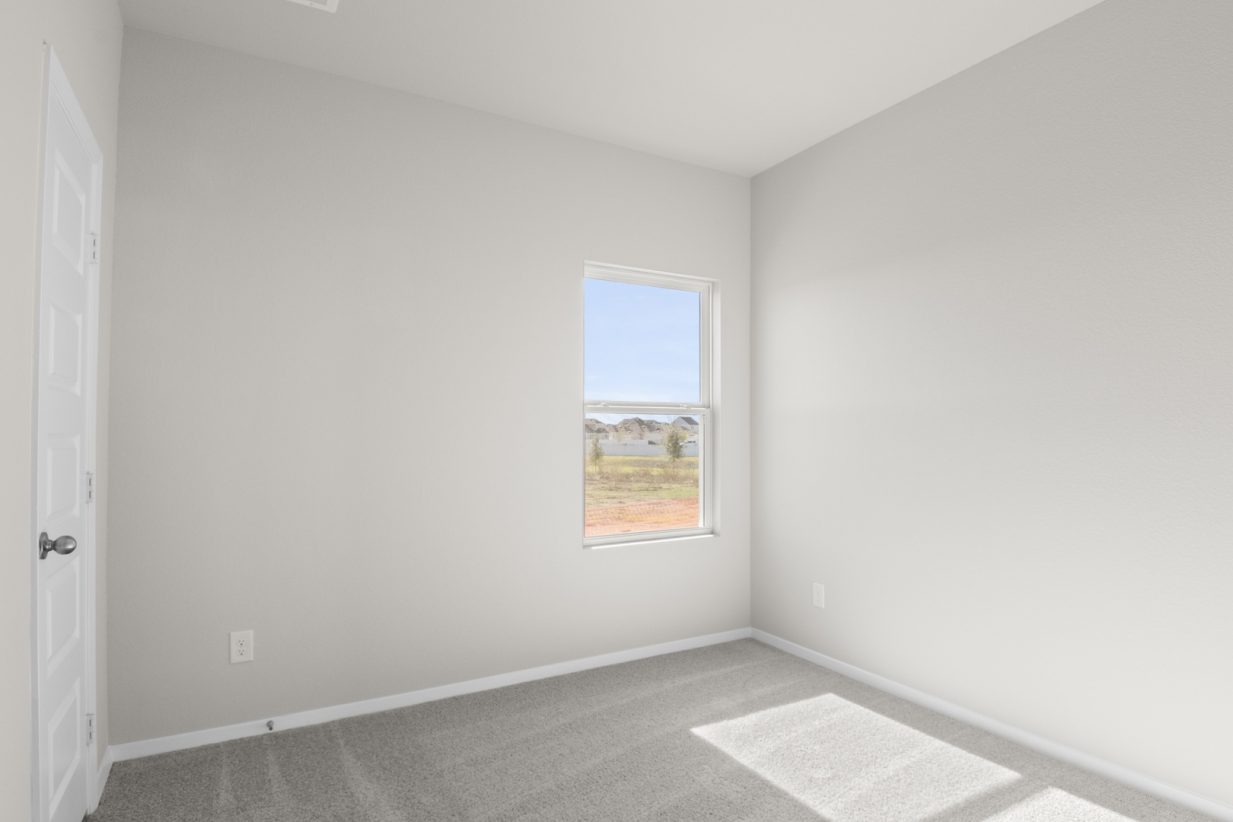 Image of a bedroom with tan carpeting and light grey walls with a window