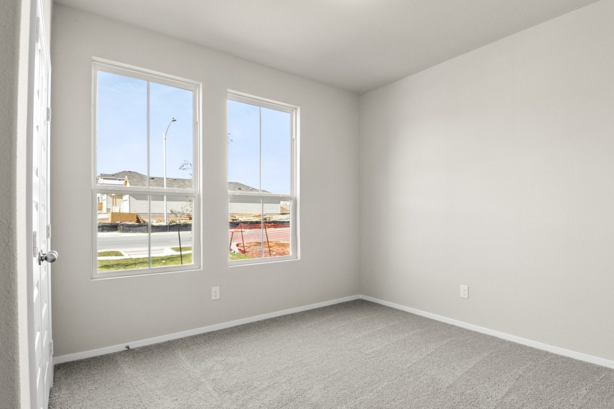 Image of a bedroom with light grey walls, two windows, and tan carpeting
