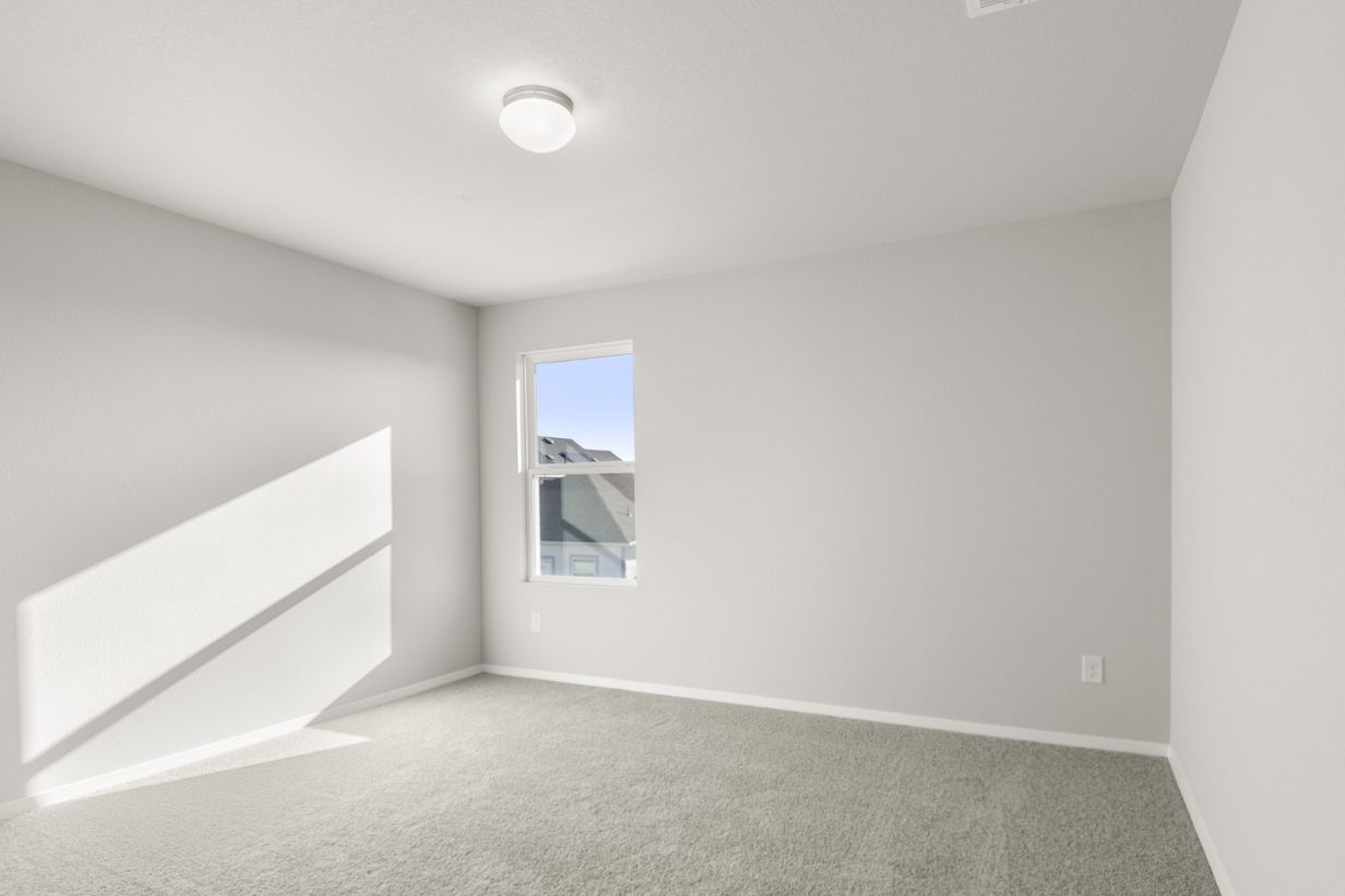 Image of a bedroom with tan carpeting and light grey painted walls with a window in the corner
